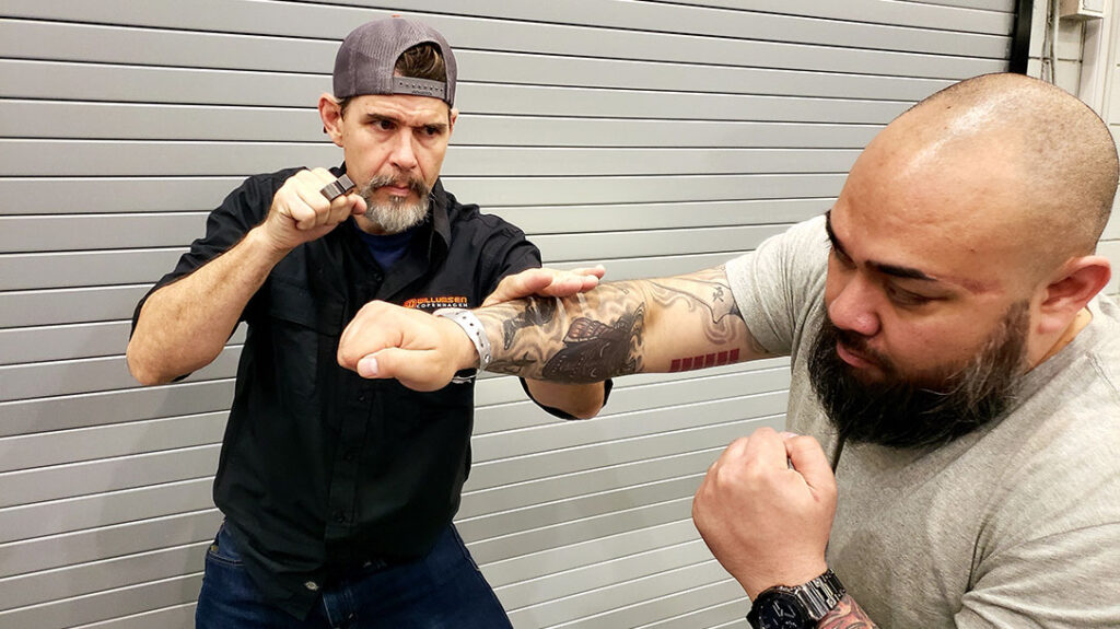 Proper Blocking: Chris successfully slaps his attacker’s strike aside, clearing an opening to deliver a straight right punch of his own. Complete with a copper knuckle.