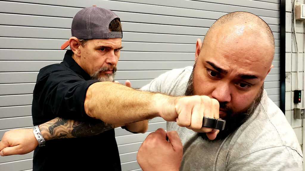 Jose attempts a right punch to Chris’s face. Chris slips an angled step to the outside of Jose’s strike while delivering a parry to counter the strike, pushing and slapping it aside and creating an opening for a counter.