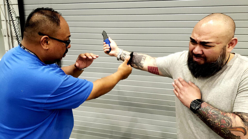 Jose attempts a right-handed knife slash at Frank. Frank steps out into the right (V-Step Angle 1) and delivers a counter-cut block to Jose’s attacking forearm.