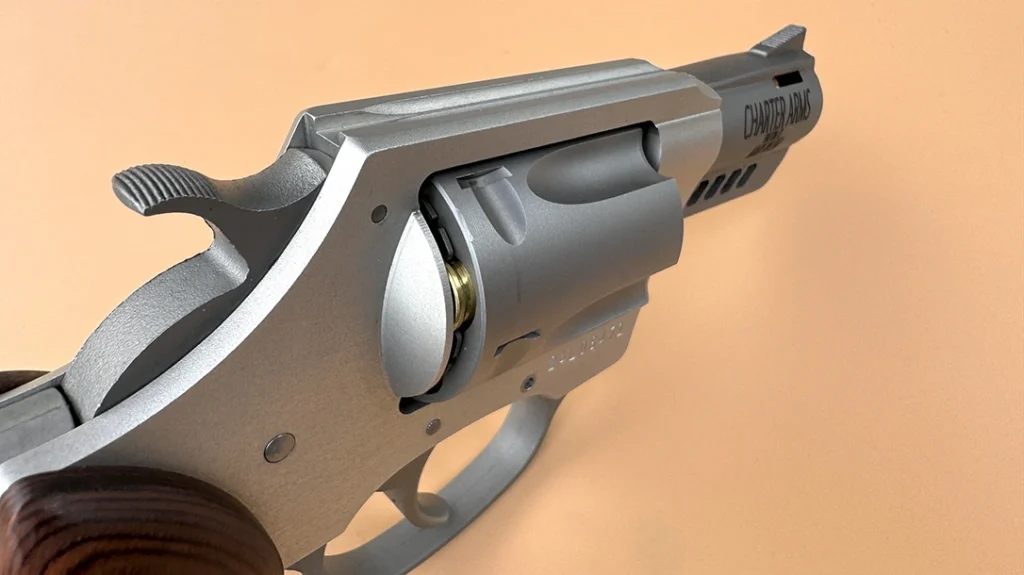 Here, you can see the fixed rear sight, the serrated ramp front sight, serrated hammer spur, plus note the slot barrel port near the muzzle.