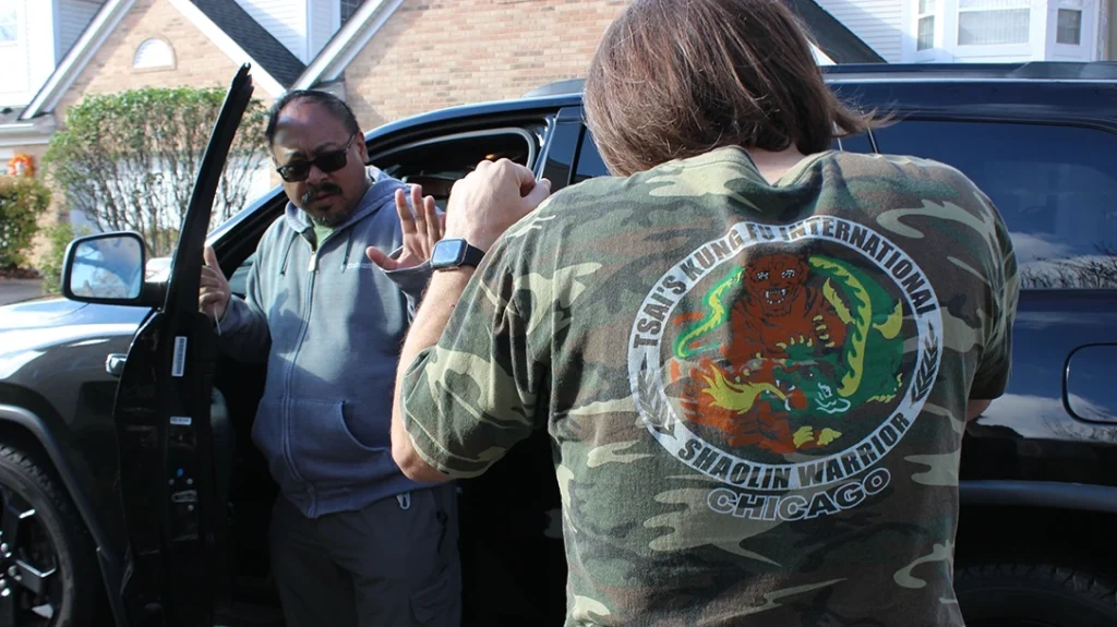 Don aggressively approaches Frank’s Vehicle. Frank puts a hand out toward Don and attempts to de-escalate the situation. Frank is holding a small screwdriver in his right hand.